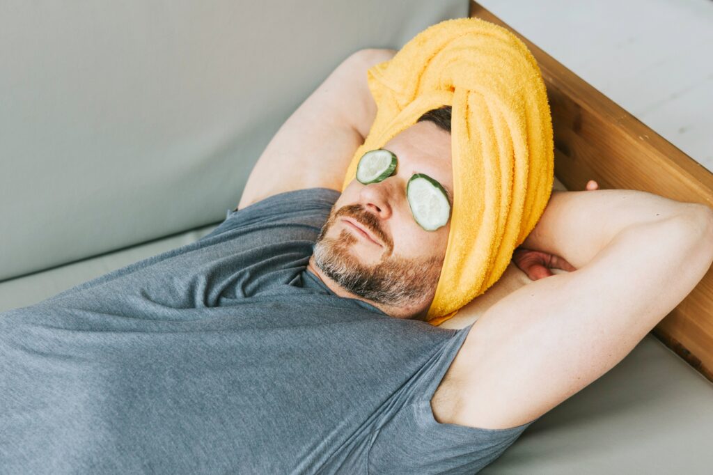 Man lying down and treating himself with cucumber on his eyes.  Obviously feeling relaxed after having hypnotherapy from Emma Rose-Roberts